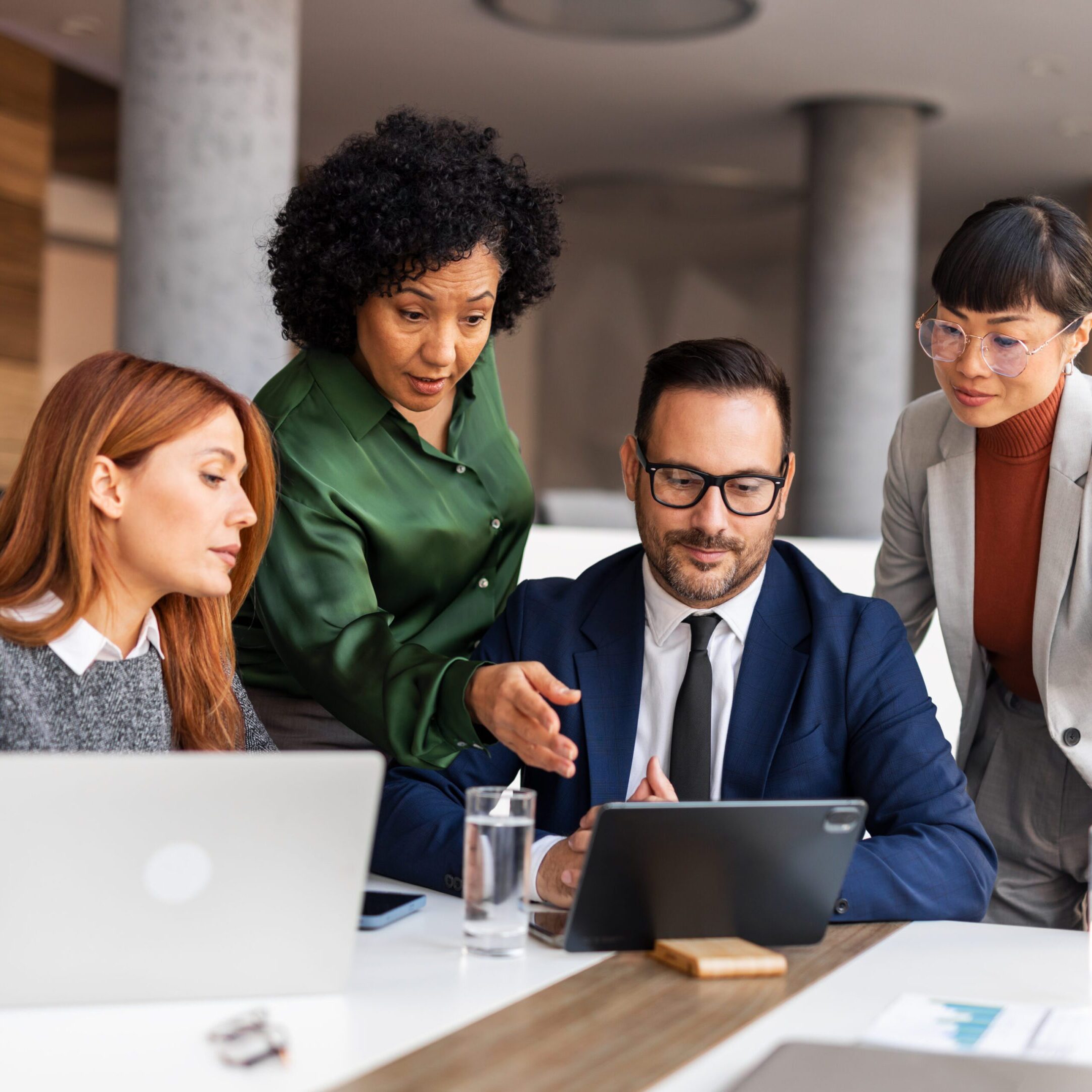 Four professionals collaborating over a tablet in a modern office.