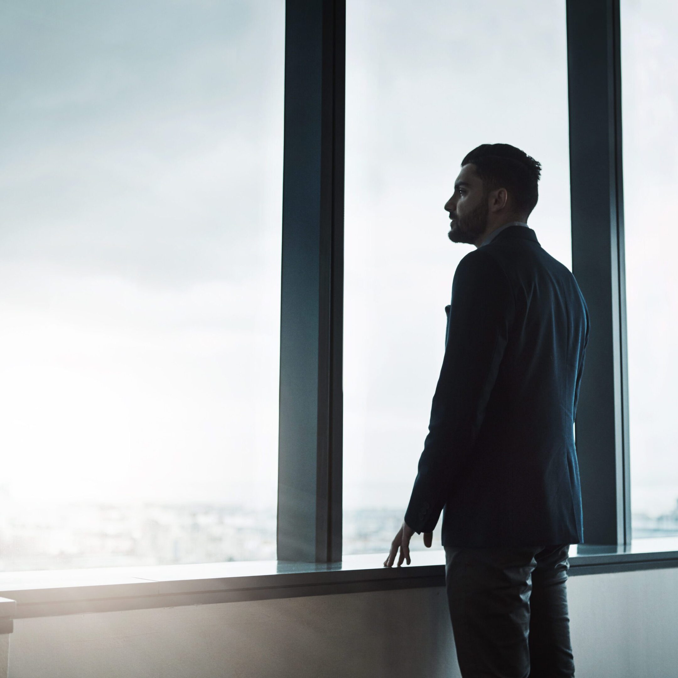 Man in suit gazing out a large window at cityscape.